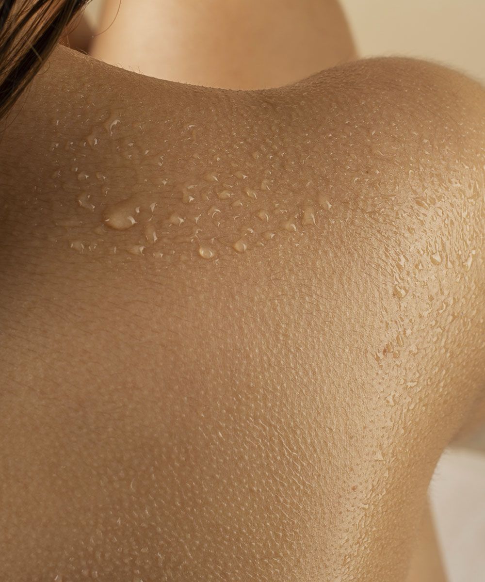 Primo piano di pelle della spalla con gocce d’olio che evidenziano idratazione e texture naturale