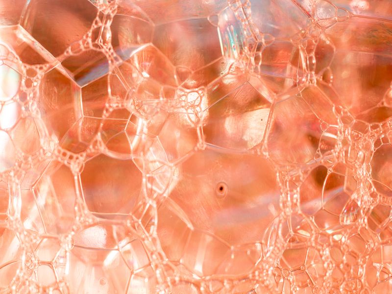 Dettaglio macro di bolle trasparenti color pesca, con riflessi luminosi che evocano la texture di una sostanza cosmetica o biologica.