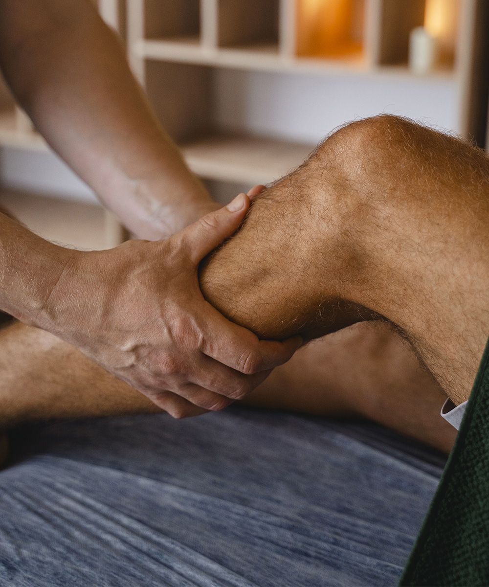 Primo piano di un massaggio a un ginocchio, con mani che applicano pressione per favorire il sollievo muscolare.