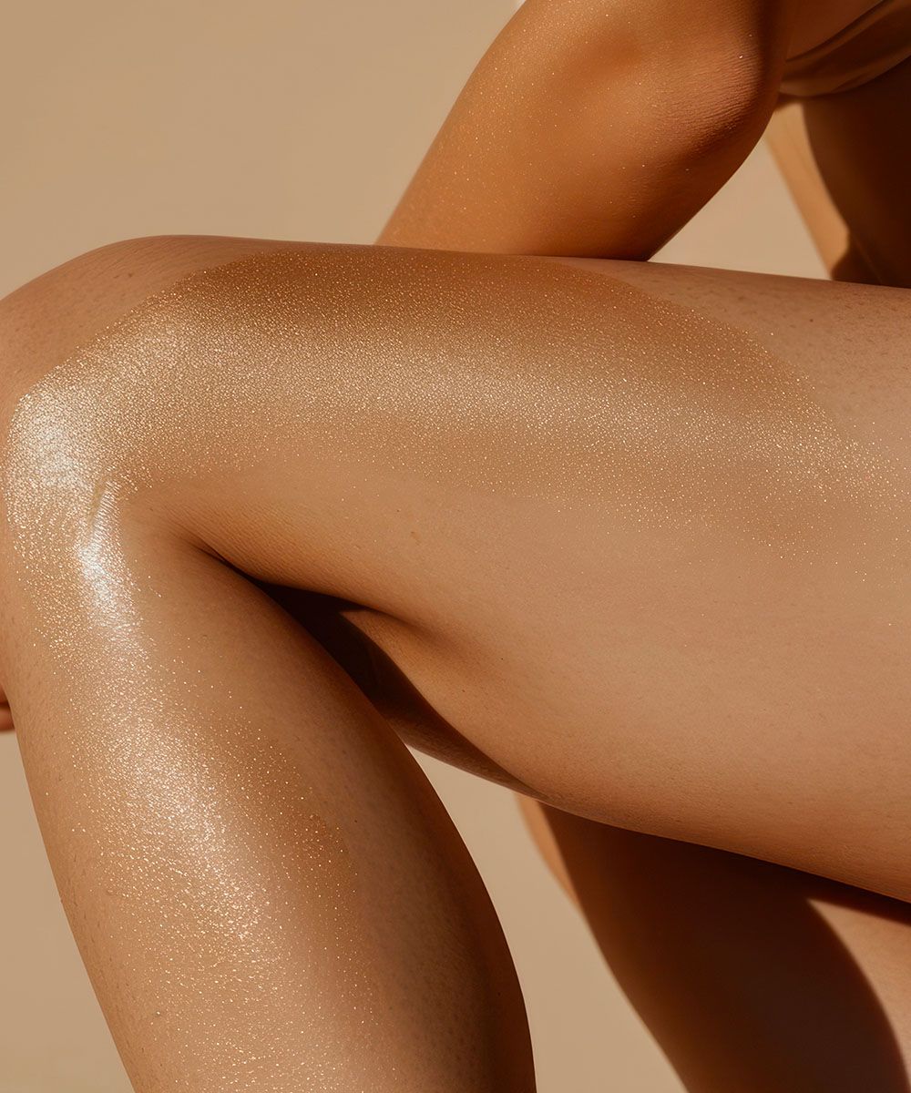 Primo piano di gambe illuminate da luce calda, con pelle lucida e idratata dopo l’applicazione di olio corpo.
