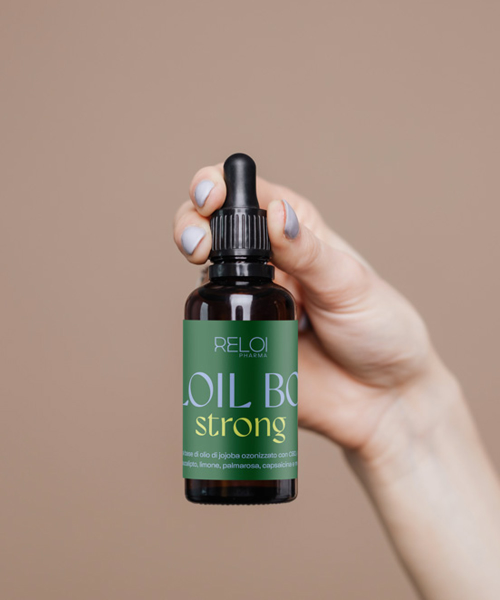 Primo piano di una mano che tiene un flacone ambrato di Reloil Body Strong con etichetta verde scuro e gialla.