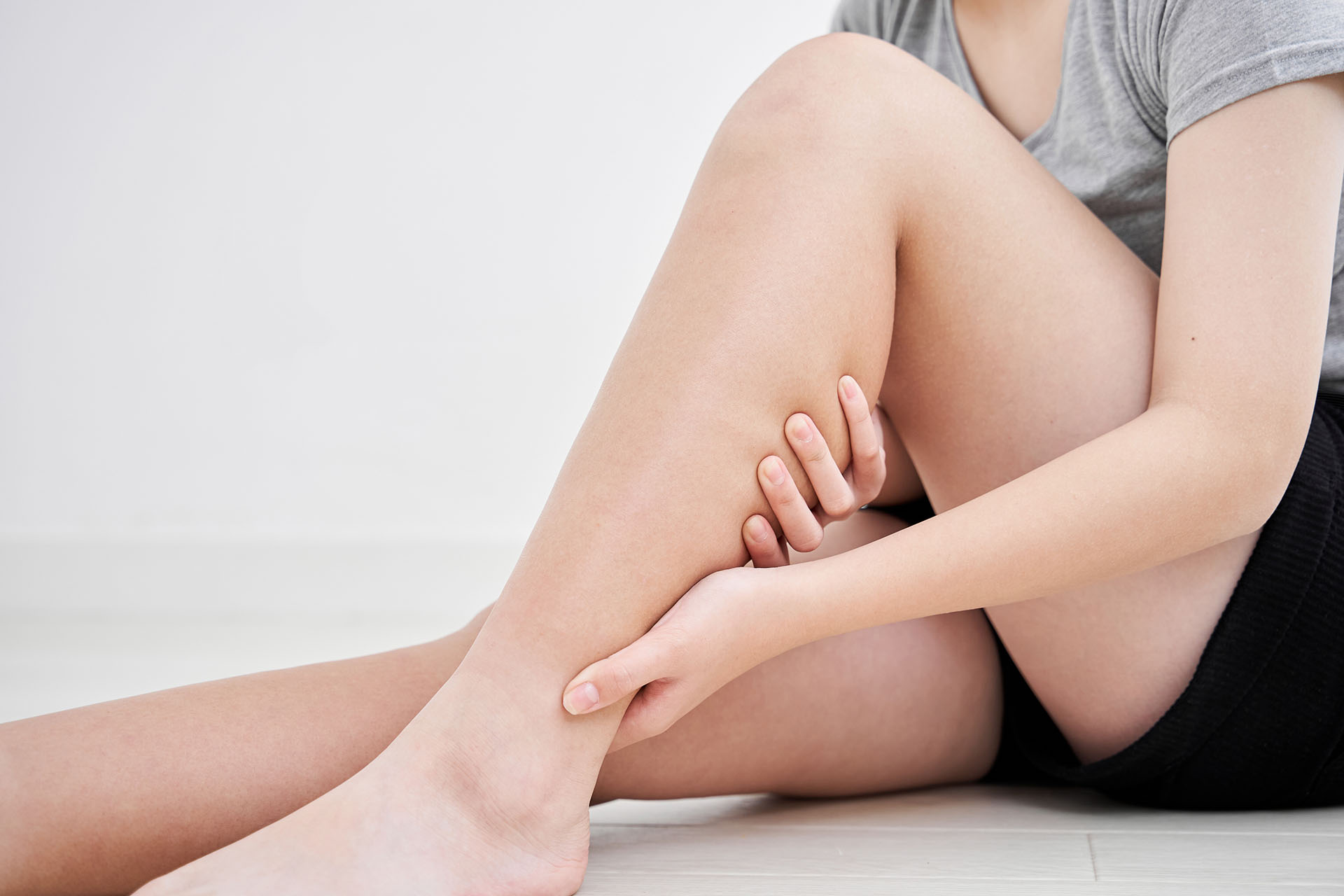 Donna seduta massaggia il polpaccio, segni di ritenzione idrica e cellulite.