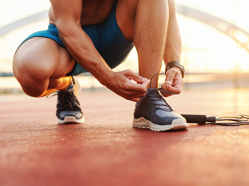 Atleta si allaccia le scarpe da corsa su pista sportiva al tramonto