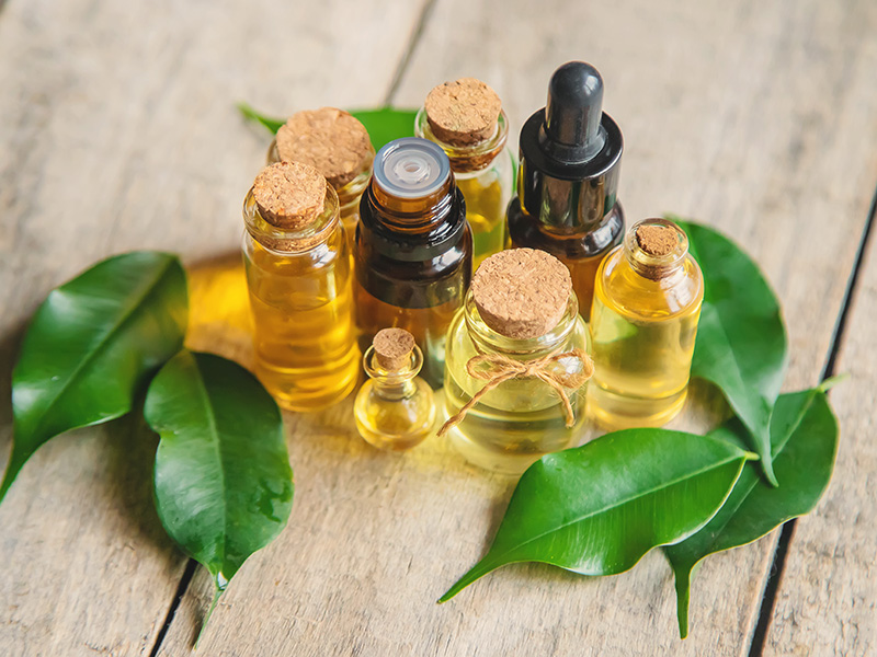 Collezione di flaconi in vetro contenenti oli essenziali per uso sportivo e benessere naturale, disposti su superficie in legno con foglie fresche, simbolo di aromaterapia e rimedi naturali