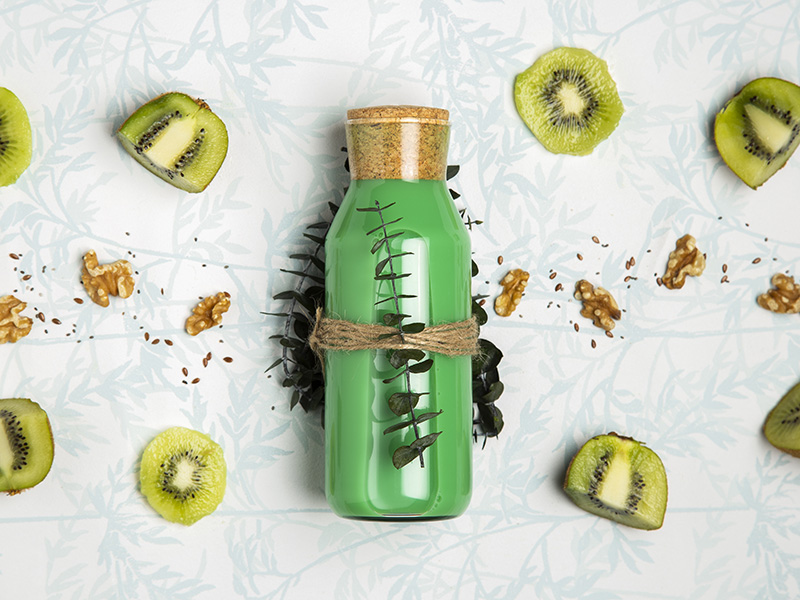 Integratore naturale in bottiglia decorata con foglie ed elementi vegetali, affiancato da ingredienti salutari come kiwi, noci e semi, simbolo di uno stile di vita sano e sportivo