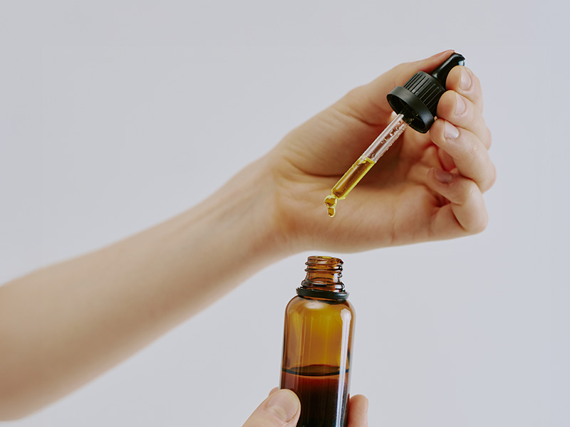 Applicazione di olio rassodante con contagocce da boccetta in vetro ambrato.