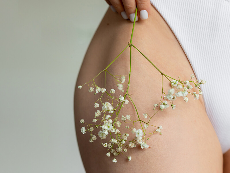 Gamba femminile con fiore delicato: simbolo dell’azione antinfiammatoria naturale della PEA negli oli corpo rigeneranti.