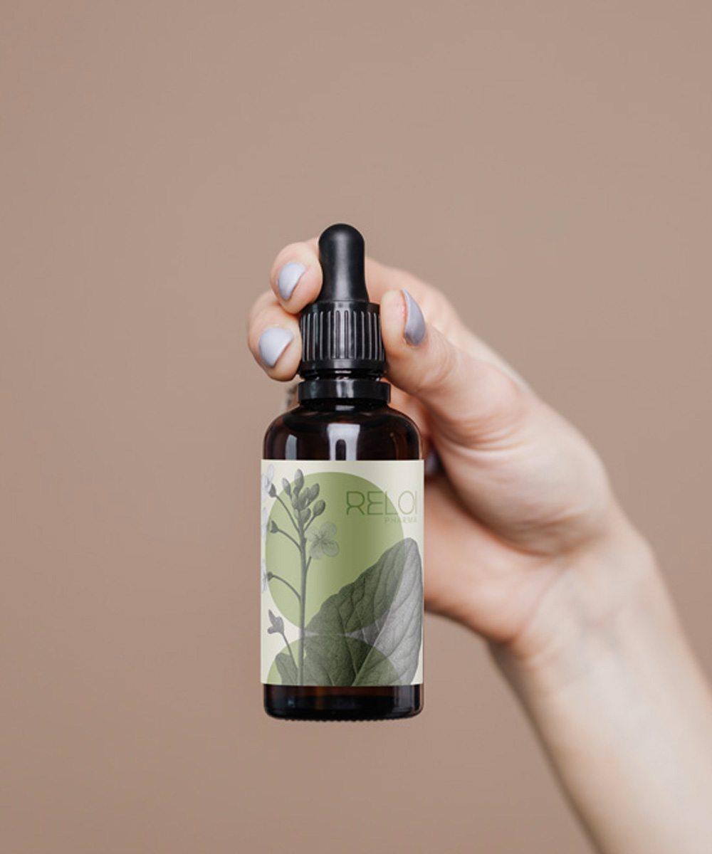 Primo piano di una mano che impugna un flacone ambrato di Kaïos Body Oil con etichetta bianca e verde decorata da illustrazioni botaniche.