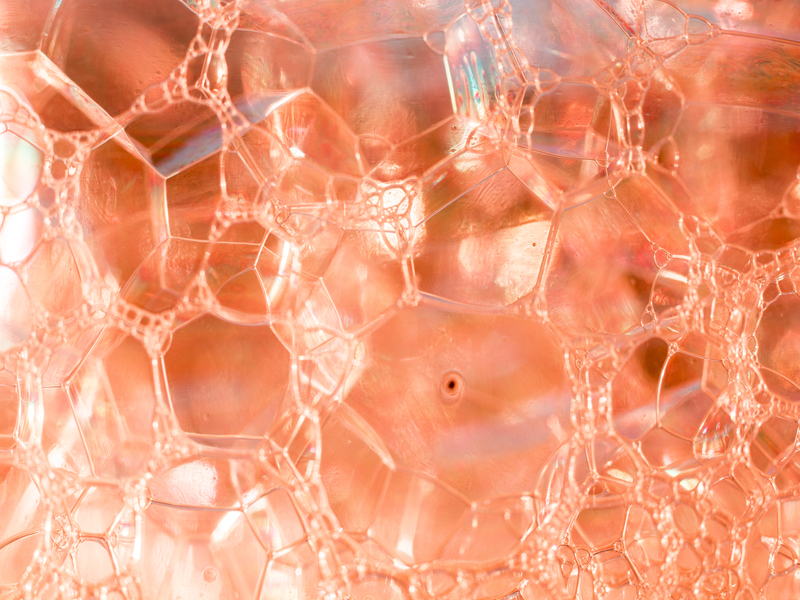 Dettaglio macro di bolle trasparenti color pesca, con riflessi luminosi che evocano la texture di una sostanza cosmetica o biologica.