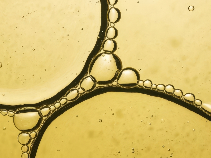 Macro fotografia astratta di bolle d’olio e acqua su fondo giallo dorato, con linee scure fluide e texture luminosa.
